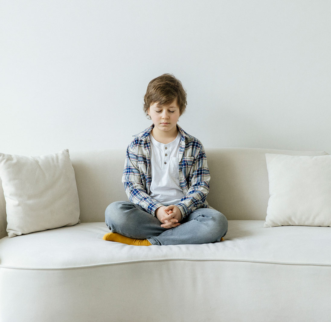 мальчик практикует Трансцендентальную Медитацию сидя на диване